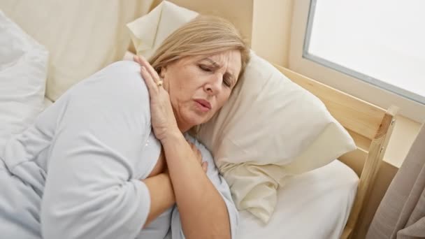 Uma mulher de meia-idade na cama cobrindo-se com um edredom, sentindo frio em um quarto brilhante. - Filmagem, Vídeo