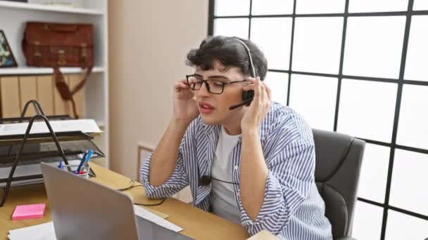 Een gestresste jongeman met een headset aan zijn rommelige bureau toont bezorgdheid terwijl multitasking. - Video