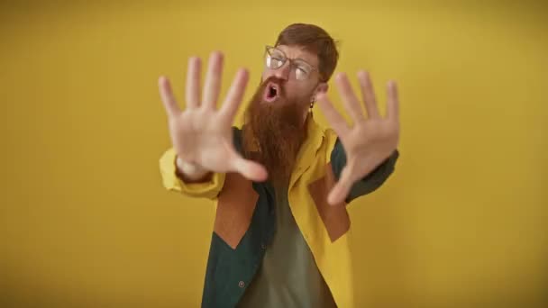 Gefrustreerde jonge roodharige man in bril en shirt, staand over geïsoleerde gele achtergrond, een vurig 'stop' gebaar makend met zijn handen, woede op zijn gezicht geschilderd. - Video