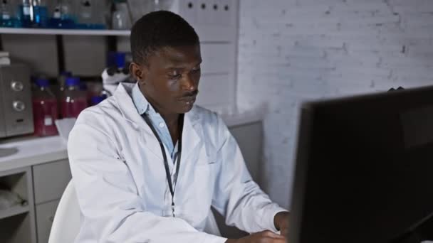 Hombre africano con bata de laboratorio trabajando en la computadora en un moderno entorno de laboratorio - Metraje, vídeo