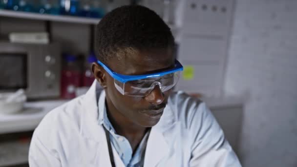 Afrikkalainen mies tiedemies yllään lab takki ja suojalasit modernissa laboratoriossa - Materiaali, video