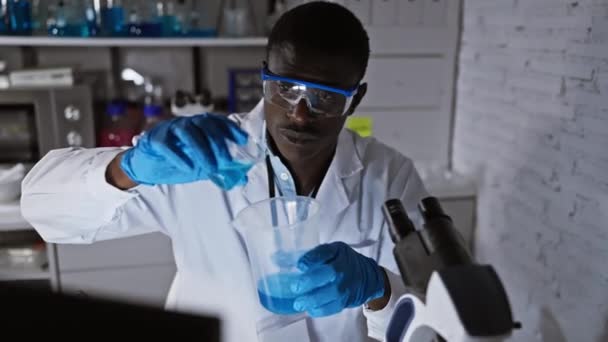 Afrikkalainen tiedemies mies tekee tutkimusta laboratoriossa ympäristössä, tarkastaa dekantterilasi sininen neste. - Materiaali, video