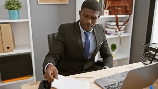 Εστιασμένος μαύρος διαβάζει έγγραφα σε ένα σύγχρονο περιβάλλον γραφείου, απεικονίζοντας τον επαγγελματισμό και τη συγκέντρωση. - Πλάνα, βίντεο