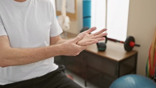 Dospělý muž vyšetřuje svou ruku na fyzioterapeutické klinice, což svědčí o zdravotní péči ve vnitřním prostředí. - Záběry, video