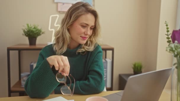 Eine fröhliche junge Frau im grünen Pullover arbeitet zu Hause mit ihrem Laptop in einem schön dekorierten Raum. - Filmmaterial, Video