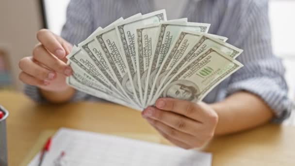 Un hombre con una camisa a rayas extiende un puñado de dólares en un ambiente de oficina, sugiriendo una transacción financiera. - Imágenes, Vídeo