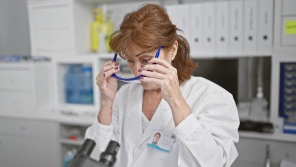 Зріла жінка-науковець коригує окуляри в лабораторному приміщенні, зображення підходить для різних медичних, дослідницьких та дорослих тем. - Кадри, відео