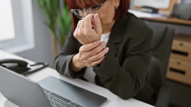Középkorú nő, akinek csuklófájdalma van az íróasztalánál, egy lehetséges munkahelyi sérülési forgatókönyvet ábrázolva.. - Felvétel, videó