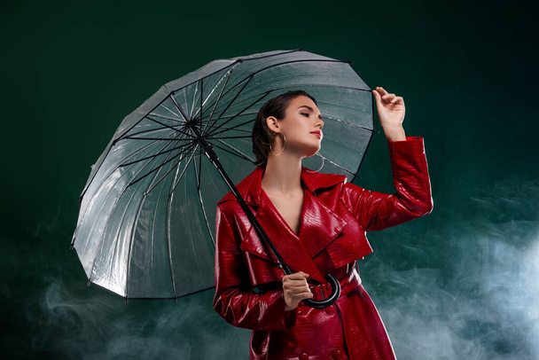 Photo of attractive girl hold umbrella wear coat look profile side isolated dark misty background. - Foto, imagen