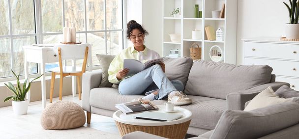 Молода жінка з журналом сидить на дивані вдома - Фото, зображення