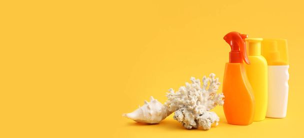 Бутылки крема от загара, ракушки и коралла на желтом фоне с местом для текста - Фото, изображение