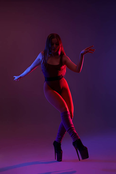 Beautiful young woman in high heels dancing on dark purple background - Photo, Image