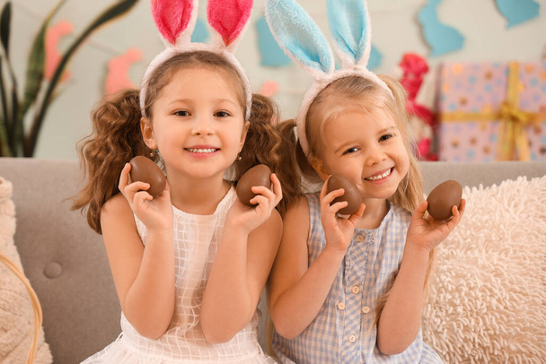 Aranyos kislányok nyuszifül csokival Húsvéti tojás ül a kanapén otthon - Fotó, kép