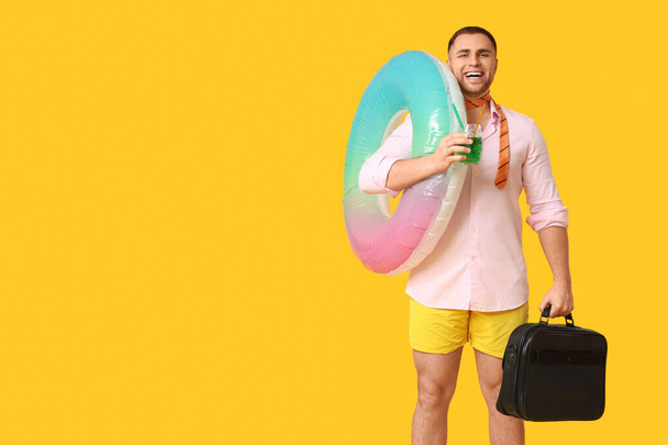 Heureux employé de bureau avec anneau gonflable, cocktail et mallette sur fond jaune - Photo, image
