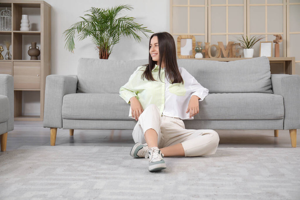 Bella giovane donna seduta al piano vicino al divano grigio in soggiorno - Foto, immagini