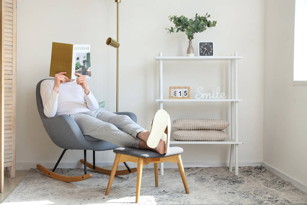 Hombre en zapatillas cómodas suaves leyendo revista en la sala de estar - Foto, Imagen