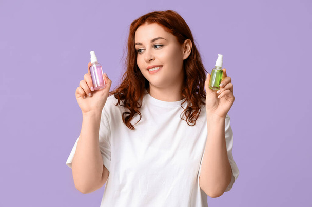 Piękna młoda szczęśliwa kobieta z butelkami środka dezynfekującego na fioletowym tle - Zdjęcie, obraz