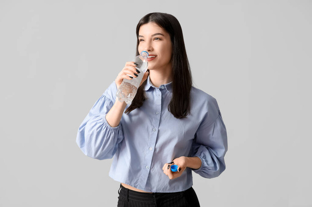 Giovane donna asiatica che beve bottiglia d'acqua su sfondo grigio - Foto, immagini