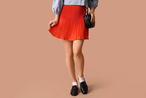Legs of beautiful young woman wearing orange mini corrugated skirt on beige background - Photo, Image