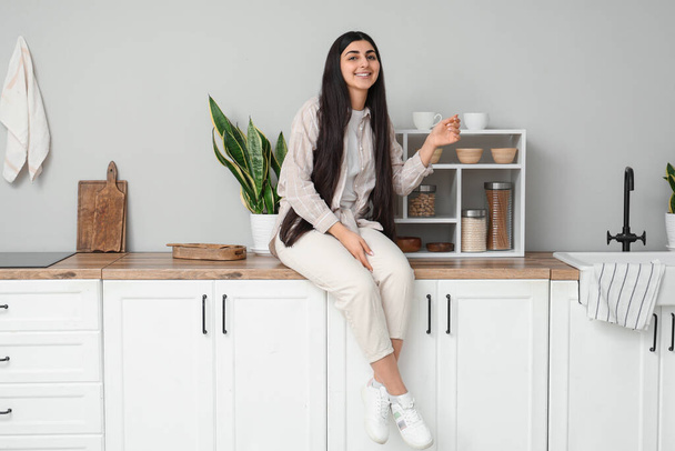 Красива молода щаслива жінка сидить на столі на кухні вдома - Фото, зображення
