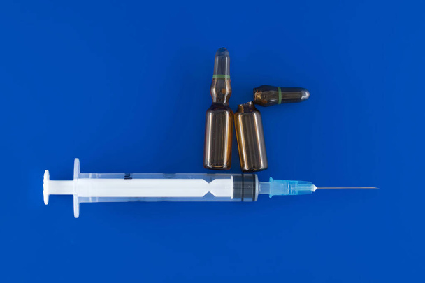 Nadel, Spritze und zwei braune Impfampullen vor blauem Hintergrund, medizinische Behandlung und Impfung - Foto, Bild