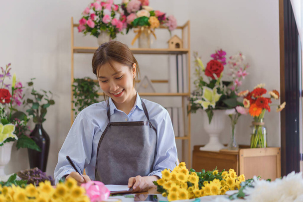 花屋のコンセプト、女性の花屋はフラワーショップでノートブックに注文や顧客情報を書く. - 写真・画像