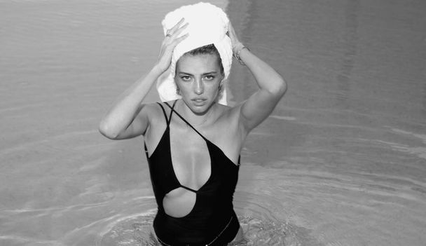 Woman with towel on head in pool water. Summer woman. Elegant sexy woman with towel posing near the swimming pool water - Фото, зображення