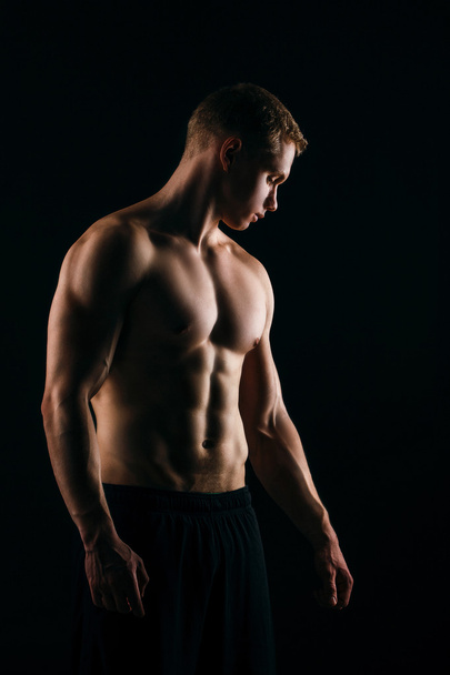 muscular young man showing his biceps isolated on black background. - Fotoğraf, Görsel