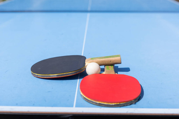 Červené a černé stolní tenis pádla a míč na modrém stolním tenisovém stole se sítí. Ping Pong koncept s kopírovacím prostorem. Kvalitní fotografie - Fotografie, Obrázek