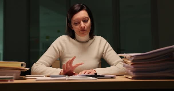 Trabajador de oficina cansado sobrecargado de papeleo tarde en la noche en la oficina. Mujer nerviosa mirando la pantalla del teléfono inteligente y esperando una llamada en la noche en el lugar de trabajo - Metraje, vídeo