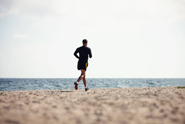 Спорт, людина і біг на відкритому повітрі для фітнесу, здоров'я і гарного самопочуття на пляжі для тренувань або фізичних вправ. Чоловік спортсмен, тренування і кардіо з витривалістю, м'язами і силою для здорового життя або спортзалу. - Фото, зображення