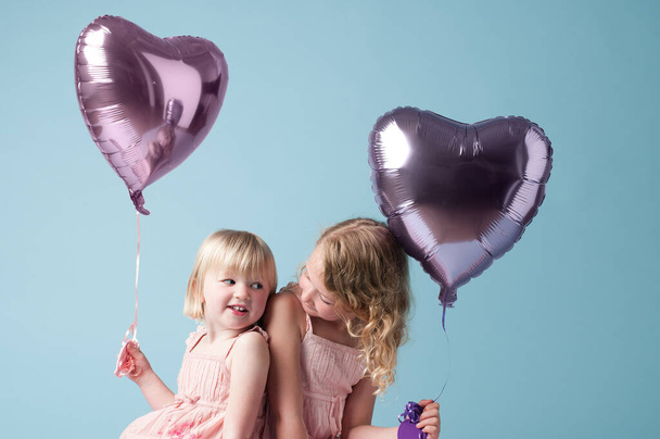 Kinderen, zus en samen met hartballon in studio op blauwe achtergrond voor familie of feestje. Verjaardag, hechting of feest met glimlach van gelukkig meisje kid vrienden op kleur achtergrond samen. - Foto, afbeelding