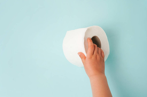 Roll bílého toaletního papíru v dětské ruce. modré pozadí s kopírovacím prostorem - Fotografie, Obrázek