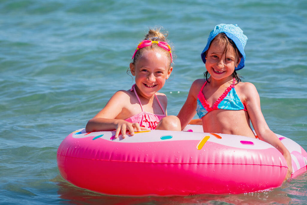 Ritratto di due belle ragazze divertenti che si divertono in mare su un cerchio gonfiabile. Vacanze estive, riposo, vacanza, persone, gioia, concetto di felicità. Immagine orizzontale. - Foto, immagini