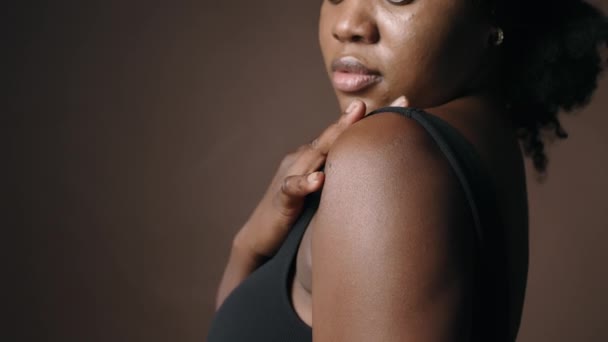 Крупним планом молода афроамериканка в чорному бюстгальтері чуттєво торкається її шкіри, позуючи в студії - Кадри, відео