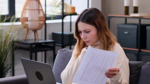 Bedachtzame en serieuze blanke vrouwelijke freelancer zittend op de bank, werkend op kantoor thuis met documenten en laptop. Studenten die online studeren. - Video