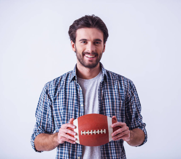 Handsome bearded man in casual clothes is holding a ball, looking at camera and smiling, on light background - Photo, Image