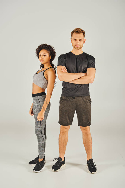 Un jeune couple sportif interracial en tenue active pose sur fond de studio gris. - Photo, image