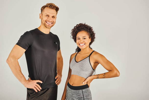 Um jovem casal esportivo interracial, vestido com desgaste ativo, marcando uma pose em um fundo de estúdio cinza. - Foto, Imagem