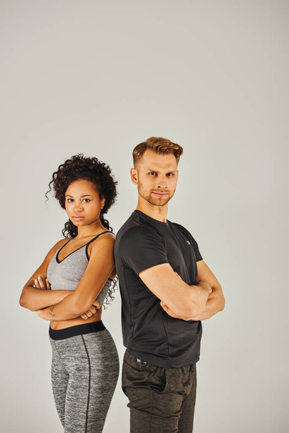 Um jovem casal esportivo interracial em desgaste ativo marcando uma pose confiante contra um fundo de estúdio cinza. - Foto, Imagem