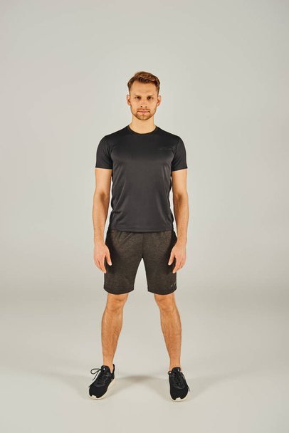 Um jovem em uma camiseta preta e shorts posa confiantemente na frente de um fundo branco. - Foto, Imagem