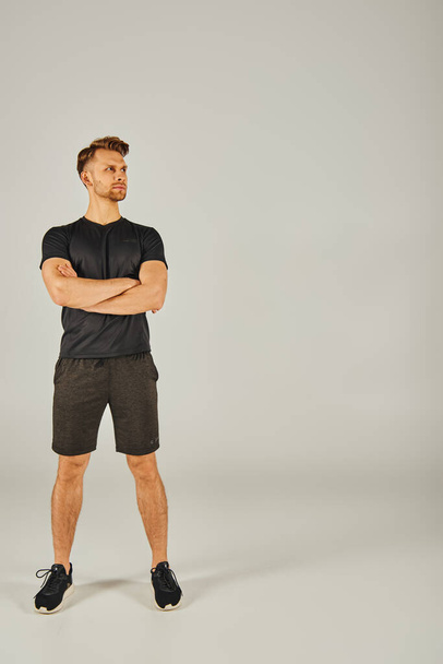 Junger, athletischer Mann in schwarzem T-Shirt und kurzen Hosen, der im Studio trainiert und Kraft und Fitness demonstriert. - Foto, Bild