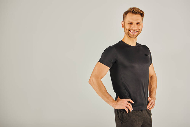 A young athletic man strikes a confident pose while wearing a black t-shirt in a studio setting. - Photo, Image