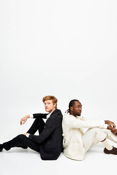 Zwei multikulturelle Männer mit feschem Stil sitzen zusammen auf dem Boden. - Foto, Bild