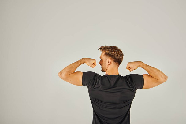 A young athletic man flexes his muscles in front of a white background, showcasing strength and determination. - Photo, Image