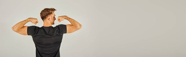 A young athletic man in active wear flexing his muscles in front of a gray background in a studio. - Photo, Image