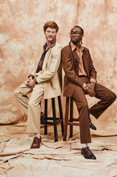 Multikulturelle Männer in eleganter Kleidung sitzen auf Holzhockern. - Foto, Bild