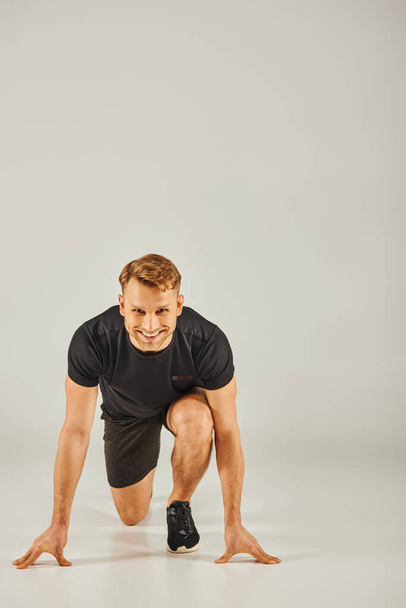 A young athletic man in active wear crouching down on a grey background in a studio setting. - Photo, Image