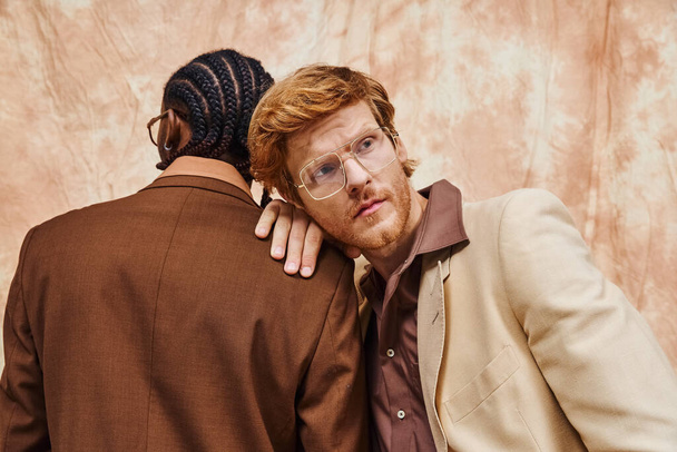 Dos hombres multiculturales vestidos con un abrazo elegante frente a una pared. - Foto, imagen