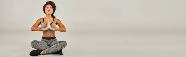 Mladá Afroameričanka v aktivním oblečení elegantně cvičí jógu na klidném šedém pozadí ve studiu. - Fotografie, Obrázek